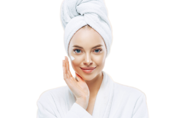 Young confident Caucasian woman applies face cream, enjoys new anti wrinkle cosmetic product, prevents sign of skin aging, wears minimal makeup, dressed in bath robe, isolated on white wall.
