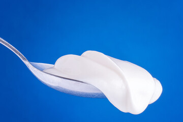 Spoon of natural yogurt and space for text on blue background