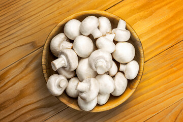 Fresh white mushrooms champignon in brown wooden bowl on wood table background