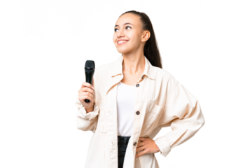 Young singer woman picking up a microphone over isolated chroma key background posing with arms at hip and smiling