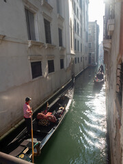 Gondoliers in gondolas in a narrow canal in Venice, Italy.