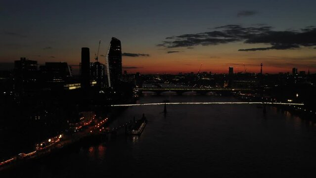 Thames river at illuminated Millennium Bridge. Silhouette of One Blackfriars skyscraper against colourful sky after sunset. London, UK