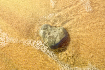 A heart-shaped stone on the shore. Sandy beach with a light sea wave. Background to a pleasant holiday, relaxing vacation and hiking in an ecologically clean area.