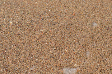 Close-up of a sea wave with white foam flowing on a pebble beach. Background with crystal clear water and sea rocks on the theme of seaside holidays and family weekends on the beach.