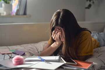 Caucasian teenage girl sitting on bed with head in hands and trying to learn