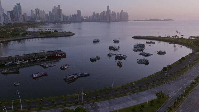 Drone cinematic shot of Panama City boats floating outside mercado de marisco in the morning by sunrise with the skyline in the background and a later tilt up to end the shot 