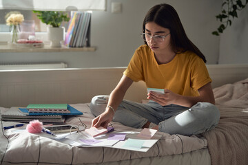 Caucasian teenage girl sitting on bed and learning from books and sticky notes