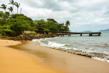 Fototapeta na wymiar Waves breaking on the sand, below the Pier, beach surrounded by rainforest in Ilhabela, Sao Paulo
