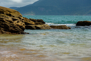View of the rocky point that advances over the blue sea and mountains in the background. Ilhabela, Sao Paulo