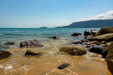 Low view of a quiet beach, gentle waves on the rocks and mountains in the background. Ilhabela, Sao Paulo
