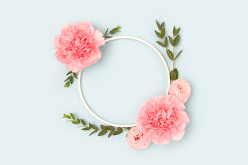 Round frame made of pink rose, carnation flowers and green eucalyptus branches on a blue...