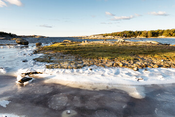 Costal winter panorama, glistering sunlight reflected in the ice and ocean, frozen beach, clear blue sky and green grass  on a beautiful clear winter day on the west-coast of Sweden