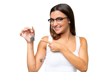Young caucasian woman holding home keys isolated on green chroma background and pointing it