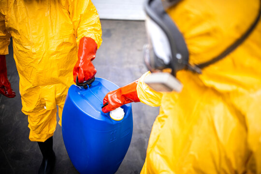 Distribution and transport of dangerous and hazardous chemicals. Two experienced and specialized workers in protection suit and gas mask carrying canister with acid.