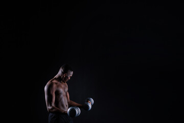 Fototapeta na wymiar Isolated african muscular man with dumbbells on dark studio background. Strong shirtless black guy