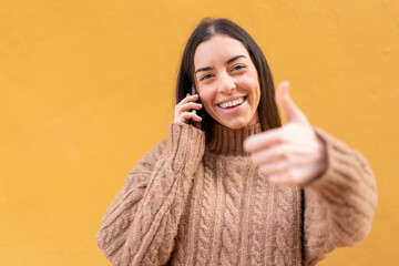 Young brunette woman at outdoors keeping a conversation with the mobile while doing thumbs up