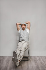 Confident young man dressed in stylish retro clothes sitting on chair