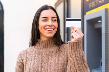 Young woman holding a credit card at outdoors with happy expression