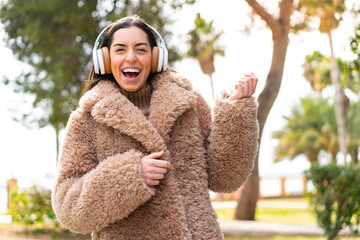 Young brunette woman at outdoors listening music and doing guitar gesture