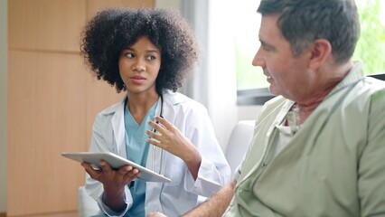 African American female medical doctor using digital tablet explain the symptoms to the patient after treatment or talking with old man patient in the hospital