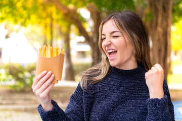 Young pretty Romanian woman holding fried chips at outdoors celebrating a victory
