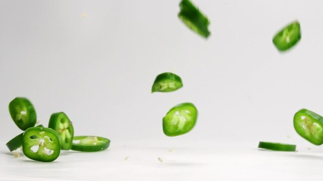 Sliced jalapeño coins falling and bouncing on white studio backdrop in 4k slow motion