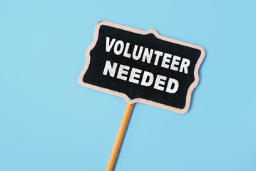 VOLUNTEER NEEDED - text on a small chalkboard on a blue background. Top view. Life and business...