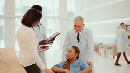 Obraz premium Two multiracial doctors are taking African patient who sitting on a wheelchair to hospital reception to take her history. A female patient receive care from male and female physicians at the hospital.