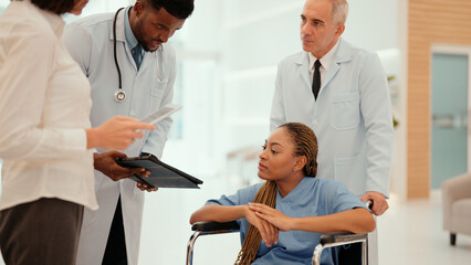 African young adult doctor is showing the result of medical examination of African patient and explaining details to her. A female patient receive care from male and female physicians at the hospital.