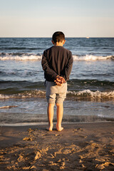 Petit garçon de dos regardant la mer prés de l'eau