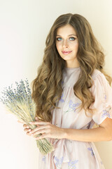 Naklejka premium Portrait of a beautiful girl with flowing curly hair, smiling, looking at the camera on on beige background. Woman with a bouquet of lavender in her hands. High quality photo