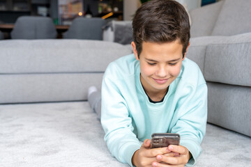 smiling boy lying on the floor facing the camera and looking at the smartphone.