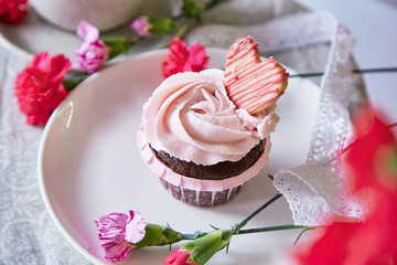 Fototapeta na wymiar Floral cupcake among flowers decoration. Escapism concept of dreamy french desserts. Spring food background.