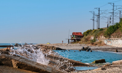 Waves break on rocks on the seashore not far from house on stilts.