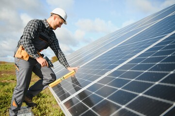 Male worker in uniform outdoors with solar batteries at sunny day.