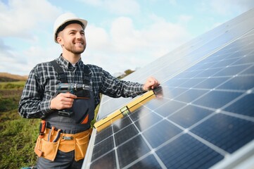 Portrait of smiling confident engineer technician with electrical screwdriver, standing in front of unfinished high exterior solar panel photo voltaic system