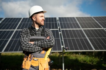 Male worker in uniform outdoors with solar batteries at sunny day.