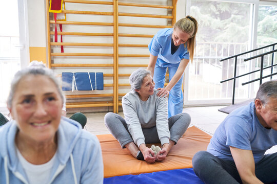 Instructor Assisting Senior Woman Practicing Cobbler Pose At Rehab Center