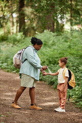 Vertical side view portrait of mother and daughter travelling in nature together and using mosquito repellent 