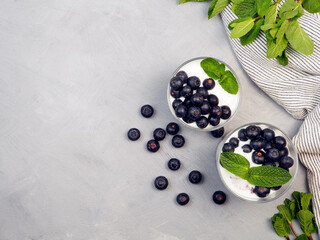 Dessert of mascarpone, blueberries and cookies in a glass decorated with mint leaves on a gray background.