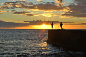 Naklejka na ściany i meble Angler stehen im Sonnenuntergang am Meer und Fischen