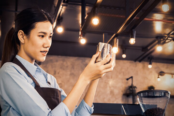 Job in coffee shop : Beautiful asian barista meticulously looks at a jug and holds jug of milk to...