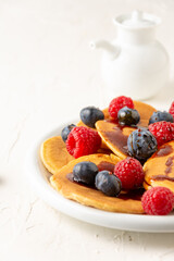 Close-up of plate of caramel pancakes with blueberries and raspberries with jar, on white table, selective focus, vertical, with copy space