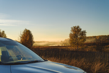 Fototapeta premium Traveling by car concept with vehicle in foreground and beautiful foggy evening landscape in background