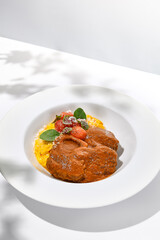 Traditional italian dish - osso buco with risotto milanese. Stew meat on bone with rice on white plate. Summer italian dining. Italian osso buco with garnish with hard shadows
