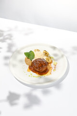 Beef cutlet with grilled cauliflower with gravy and cheese sauce on white plate. Elegant beefsteak on light background with shadows of sunlight. Summer menu with hard shadows Meat ball of minced meat