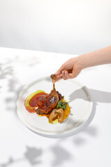 Female hand holding duck leg in restaurant. Woman eat duck confit. Eating process. Trendy food menu Hand holding duck leg on summer dining