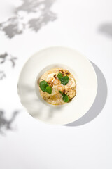 Seafood risotto with scallops and cauliflowers on white plate. Creamy risotto with sea scallops and cauliflowers. Italian risotto with sea scallops on light background with shadows of leaves