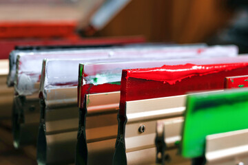 squeegees close-up on wooden shelve of the print screening apparatus. silk screen printmaking. serigraphy production. selective focus. printing images on t-shirts by silk screen method