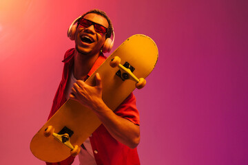 African guy posing with skateboard isolated over gradient neon background